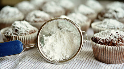 A cupcake dusted with powdered sugar rests atop a blue strainer, showcasing a delightful dessert presentation.